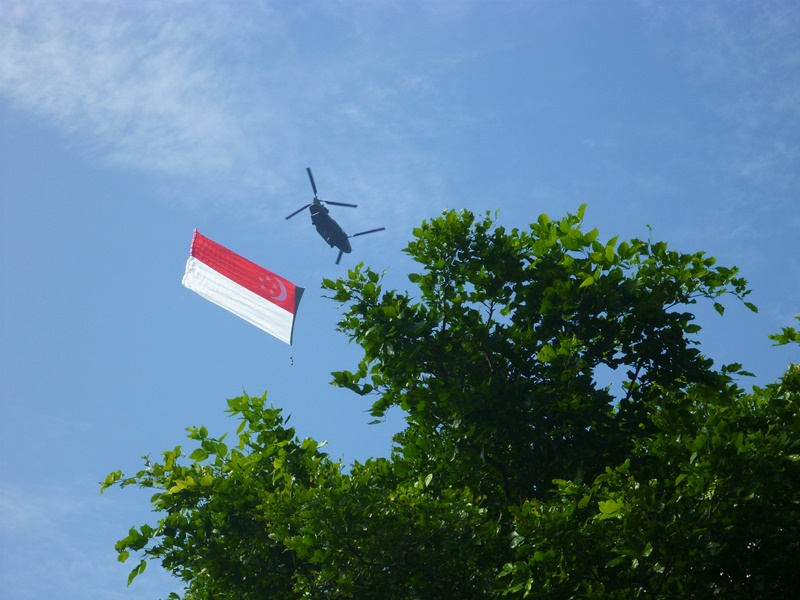 ナショナルデーパレードのリハーサルをするシンガポール国旗を掲げたヘリコプター